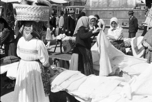 Viaggio in Jugoslavia. Zagabria: mercato. Donne croate osservano una bancarella che espone tessuti. Una reca una cesta sulla testa