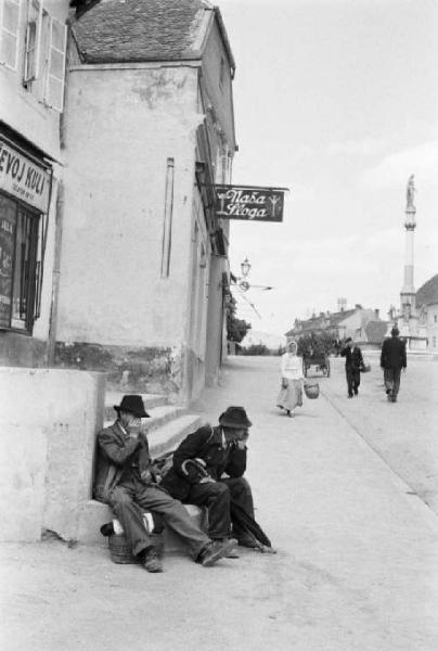 Viaggio in Jugoslavia. Zagabria: una via cittadina con due uomini seduti all'angolo della strada