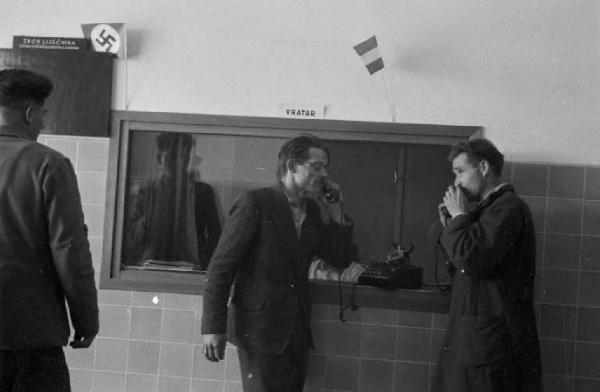 Viaggio in Jugoslavia. Ospedale di Zagabria: due uomini che parlano al telefono. Accanto una bacheca che reca la svastica nazista
