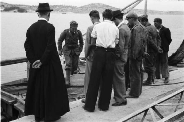 Viaggio in Jugoslavia. Sebenico: imbarcazione militare al porto - in primo piano un prete segue le operazioni di scarico della merce