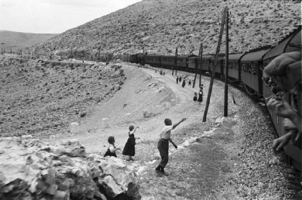 Viaggio in Jugoslavia. Verso Spalato: scorcio del paesaggio dal treno - un gruppo di bambini si avvicinano alle carrozze salutando il treno