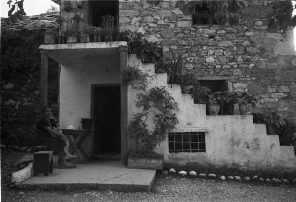 Viaggio in Jugoslavia. Mostar: scorcio di un'abitazione in pietra - sulla soglia di casa siede una donna