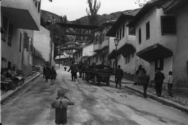 Viaggio in Jugoslavia. Sarajevo: scorcio del borgo nei pressi di un vicolo in salita - sullo sfondo si riconosce un carro adibito al trasporto merci circondato da passanti