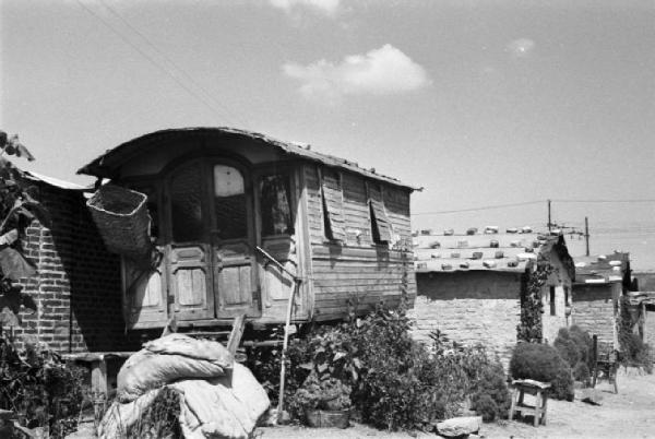 Italia Dopoguerra. Milano - Periferia - Baracche - Carrozzone adibito ad abitazione e alcune baracche