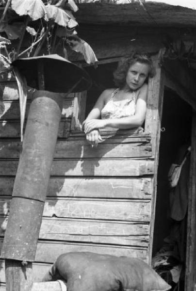 Italia Dopoguerra. Milano - Periferia - Baraccopoli - Ritratto femminile, giovane donna che si affaccia da una baracca - Norma Barbieri "la lavandaia vamp"