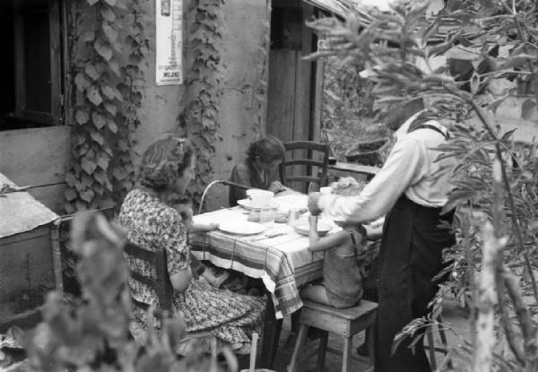 Italia Dopoguerra. Milano - Periferia - Baraccopoli - Famiglia che pranza all'esterno di una baracca
