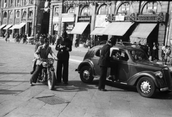 Italia Dopoguerra. Milano - Corso Buenos Aires, galleria Puccini - Coppia di vigili esegue dei controlli a un automobilista e a un motociclista