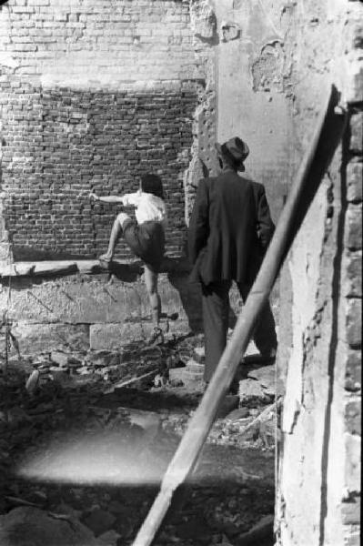 Italia Dopoguerra. Milano - Donna tra le macerie indica qualcosa al di là di un muro mentre un uomo di spalle la osserva