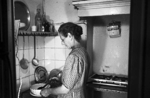 Italia Dopoguerra. Periferia di Milano, le case popolari del quartiere "Baia del Re". Interno di una abitazione, donna in cucina