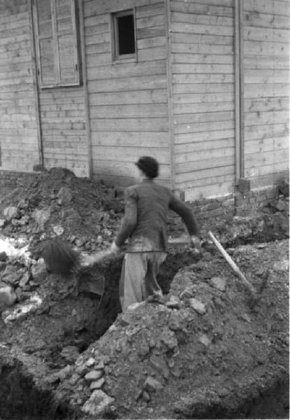 Italia Dopoguerra. Milano - Quartiere Baggio - Un uomo durante la realizzazione di un canale di scolo lungo un edificio abitativo prefabbricato