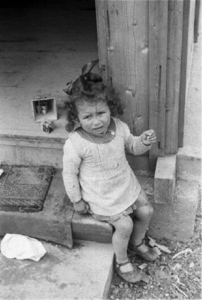 Italia Dopoguerra. Milano - Quartiere Baggio - Bambina seduta sull'uscio di casa