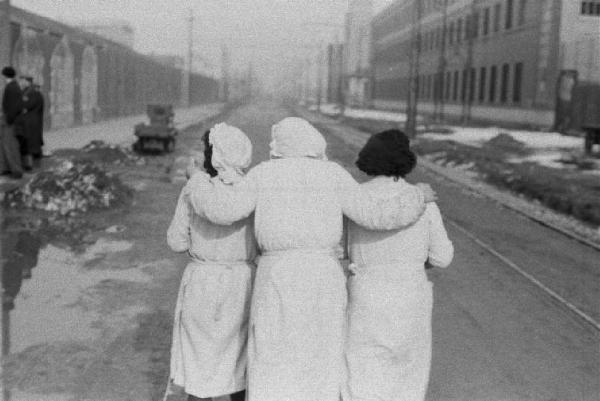 Italia Dopoguerra. Milano. Stabilimento Pirelli Bicocca. Tre donne abbracciate lungo il viale all'uscita della fabbrica
