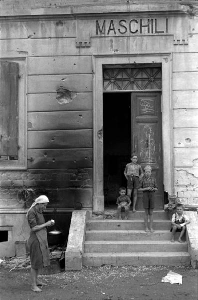 Italia Dopoguerra. Marzabotto - Scuola - Ingresso - Bambini seduti sui gradini - Donna