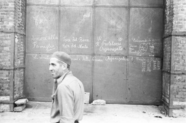 Italia Dopoguerra. Genova - Operaio passa davanti a una serranda con scritte in gesso che inneggiano al proletariato