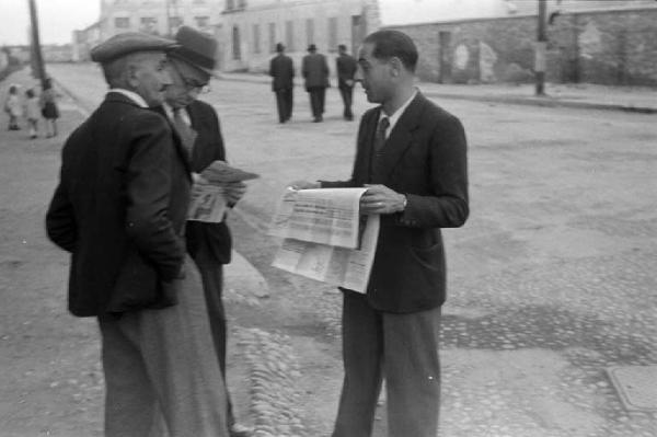 Italia Dopoguerra. Milano. Strada - Uomini discutono leggendo un giornale