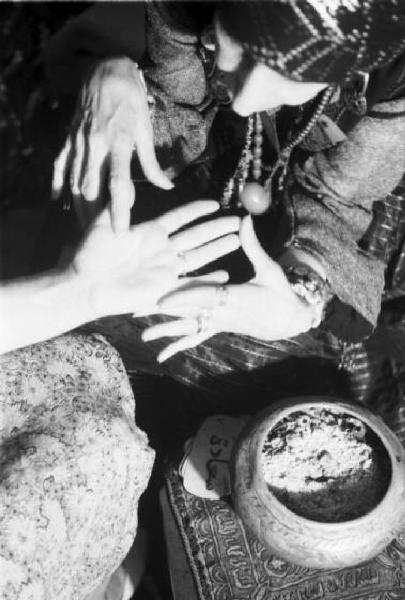 Leda Rafanelli nel suo studio legge la mano ad una donna - attorno una ciotola e tessuti orientali