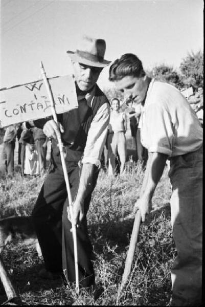 Invasione delle terre. Gruppo di contadini che manifestano in un prato. Due uomini piantano un cartello con la scritta "W i contadini"