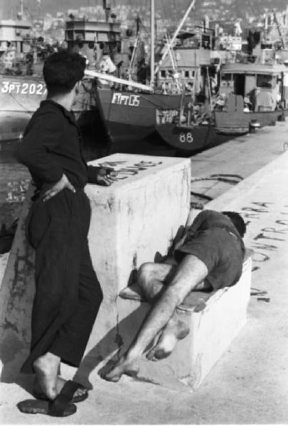 Italia Dopoguerra. Genova - Scorcio del porto con coppia di uomini di cui uno sdraiato lungo il molo