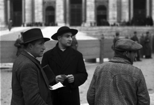 Roma. Un prete fa conversazione con una coppia di uomini in Piazza San Pietro