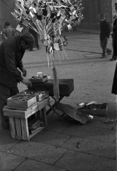 Italia Dopoguerra. Milano - fiera degli Obèi - Obèi: un venditore ambulante sistema la propria merce sopra alcune cassette di legno