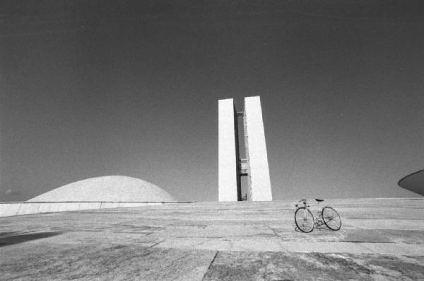 Brasilia. Bicicletta da corsa tra le due cupole del Congresso Nazionale, con il doppio grattacielo sullo sfondo
