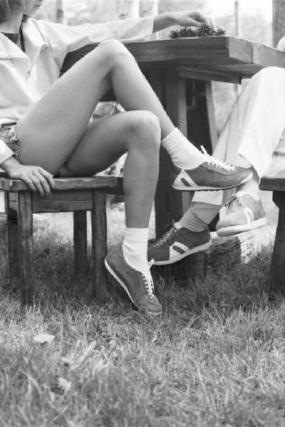 Atalasport. Gambe di una coppia che calza scarpe Atala si incrociano sotto un tavolo all'aperto