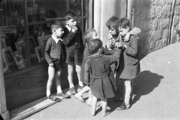 Italia Dopoguerra. Napoli. Bambini giocano lungo la strada in prossimità del negozio di un fotografo