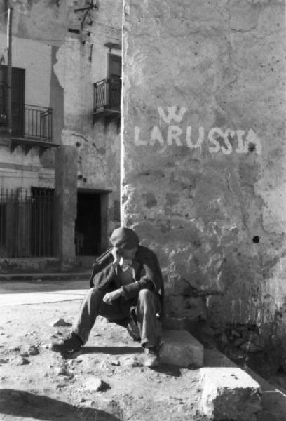 Italia Dopoguerra. Palermo. Un uomo seduto all'angolo di una strada accanto a un muro con la scritta "W LA RUSSIA"