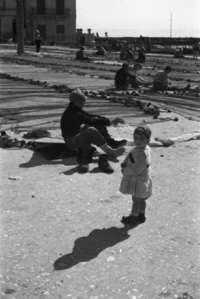 Italia Dopoguerra. Mondello. Ritratto di una bambina mentre i pescatori sistemano le reti