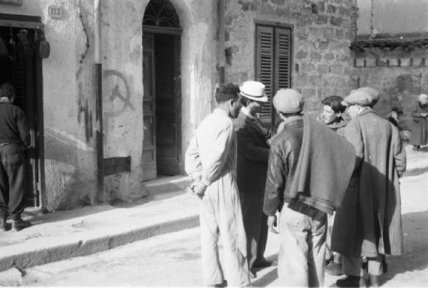 Italia Dopoguerra. Palermo. Gruppo di uomini discute davanti ad un portone a lato del quale è disegnata una falce con martello