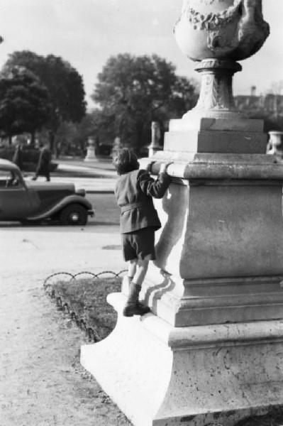 Parigi. Un bambino gioca arrampicandosi e nascondendosi dietro il basamento di un monumento