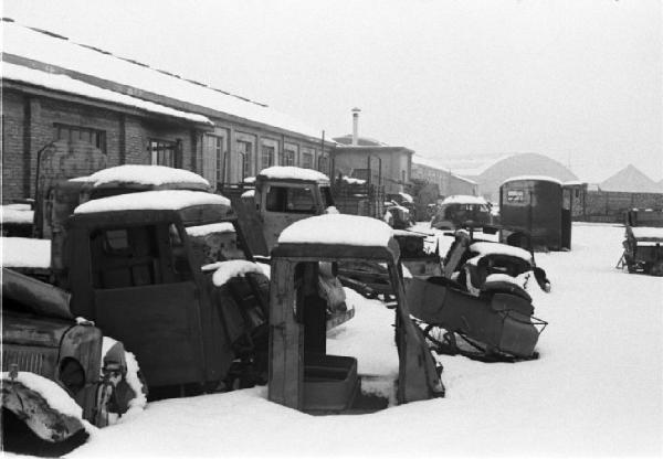 Carcasse di automezzi abbandonati nella neve all'esterno di un capannone industriale