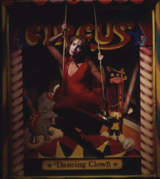 Fotomodella in abito rosso posa su altalena - sullo sfondo una locandina di circo