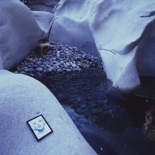 Val Verzasca - fotomodella nuda all'interno di una conca ghiaiosa - in primo piano, appoggiata sopra uno scoglio, una riproduzione del viso di Marilyn Monroe