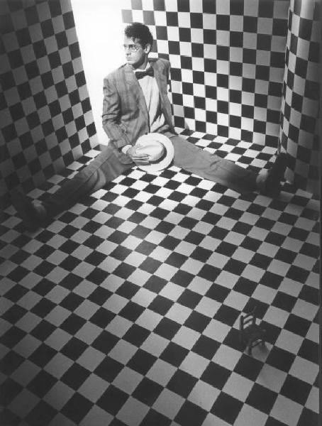 Moda maschile. Ritratto in studio - fotomodello in posa seduto a terra indossa un completo giacca e pantalone con farfallino e cappello