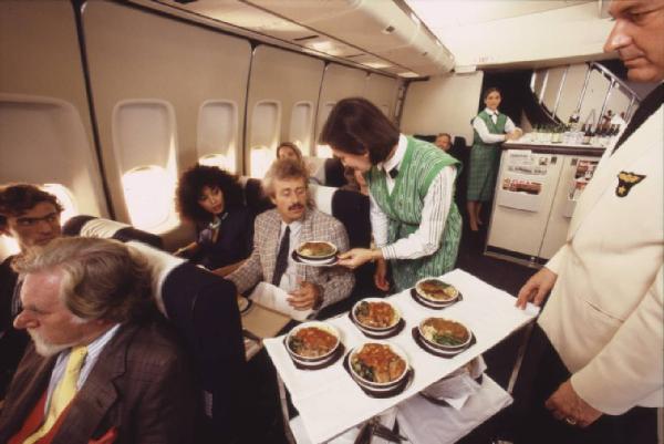 Alitalia. Interno della economy class di un aeromobile - passeggeri e hostess durante il servizio pranzo