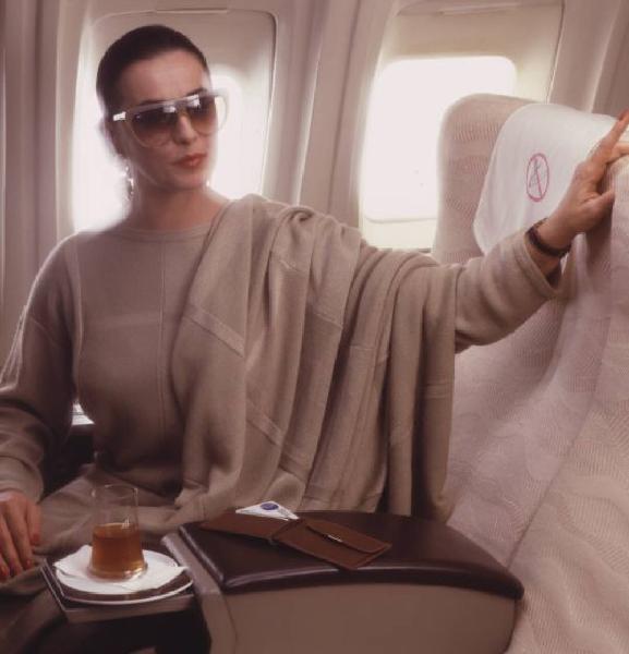 Campagna pubblicitaria Alitalia. Interno di aeromobile - business class - passeggera con tazza di tè e portafoglio