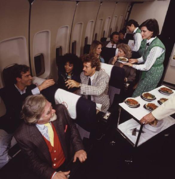 Alitalia. Interno della economy class di un aeromobile - passeggeri e hostess durante il servizio pranzo