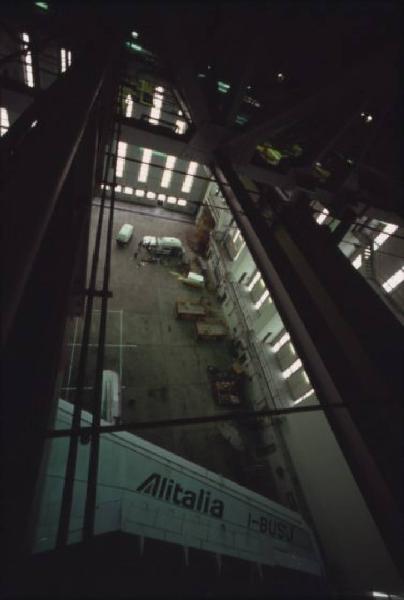Alitalia. Interno di un hangar - struttura a travi reticolari. In secondo piano un aeroplano della compagnia di bandiera con il logo sull'ala