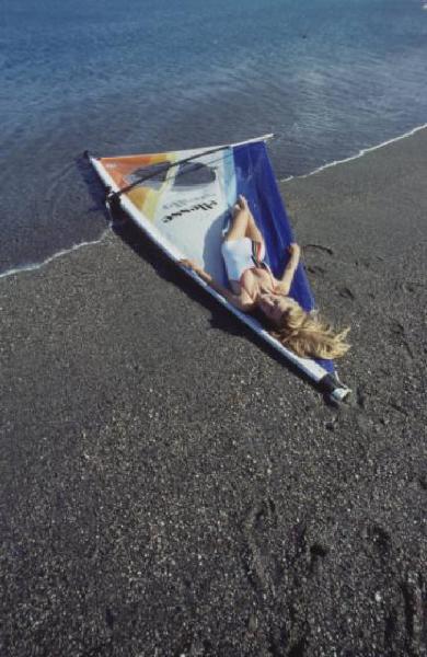 Campagna pubblicitaria Ellesse. Fotomodella indossa costume da bagno intero bianco - vela di un windsurf