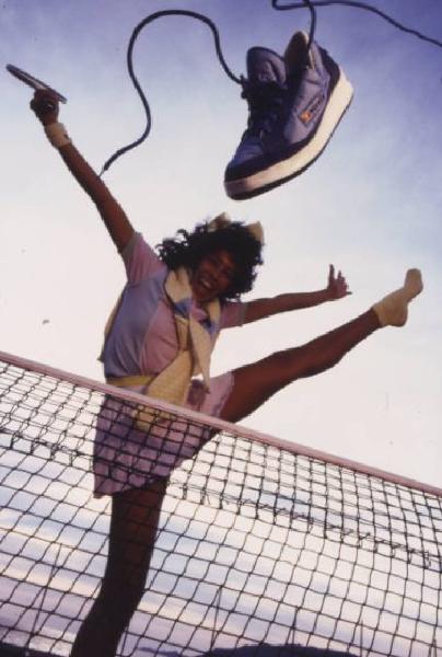 Campagna pubblicitaria Ellesse. Fotomodella indossa completo da tennis -  rete di un campo da tennis - scarpa da tennis