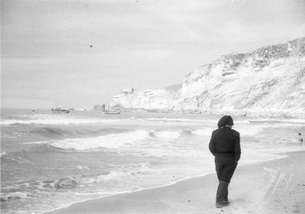 Spiaggia di Nazaré - uomo passeggia lungo la riva. Sullo sfondo la falesia