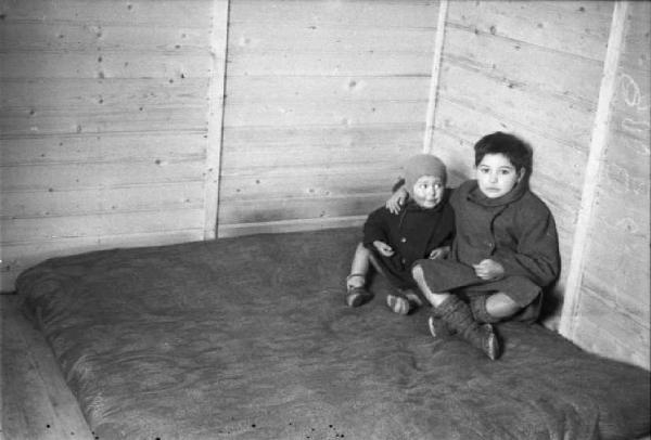 Italia Dopoguerra. Milano - Quartiere Baggio - Coppia di fratellini abbracciati sul letto della loro abitazione