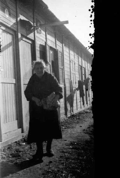 Italia Dopoguerra. Milano - Quartiere Baggio - Donna anziana cammina lungo le abitazioni prefabbricate