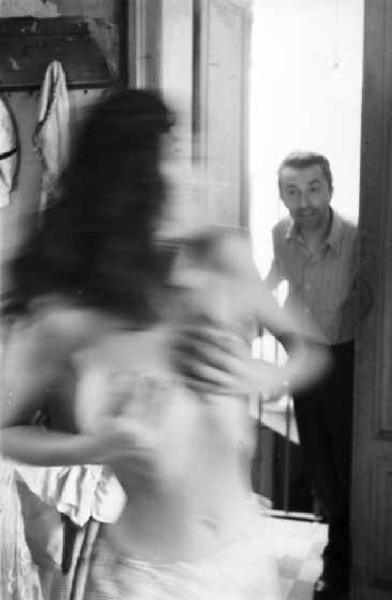 Giovane ragazza in camerino si copre il seno sorpresa da un uomo che apre la porta