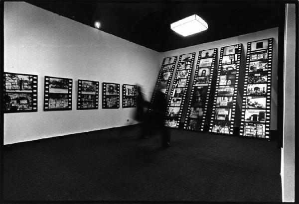 Galleria d'arte - Mostra fotografica di Aldo Tagliaferro - Visitatori in movimento al centro della sala - Alle pareti le immagini montate in striscia