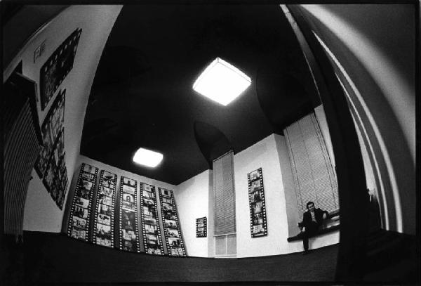 Galleria d'arte - Mostra fotografica di Aldo Tagliaferro - Alle pareti le immagini montate in striscia- uomo seduto su di una panca della sala