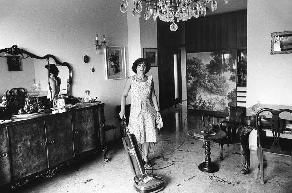 Una, nessuna, centomila. La Casa e i Riti. Milano - Salotto, interno - Mobili in legno - Specchio - Ritratto femminile: donna con aspirapolvere