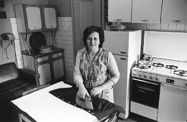 Una, nessuna, centomila. La Casa e i Riti. Milano - Cucina, interno - Ritratto femminile: donna con ferro da stiro stira una camicia sul tavolo