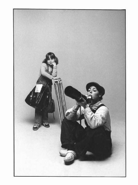I Ruoli. Ritratto di coppia: Marzia Malli con una macchina fotografica in mano e una bambina appoggiata a un treppiedi